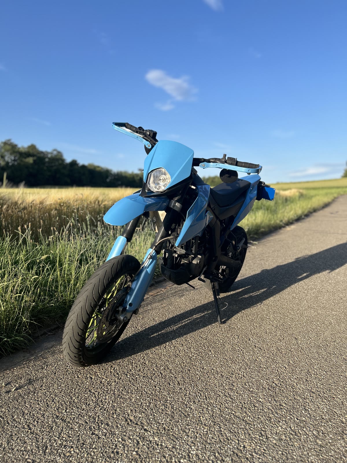 Blaues Aprilia-Motorrad auf einem Feldweg unter blauem Himmel