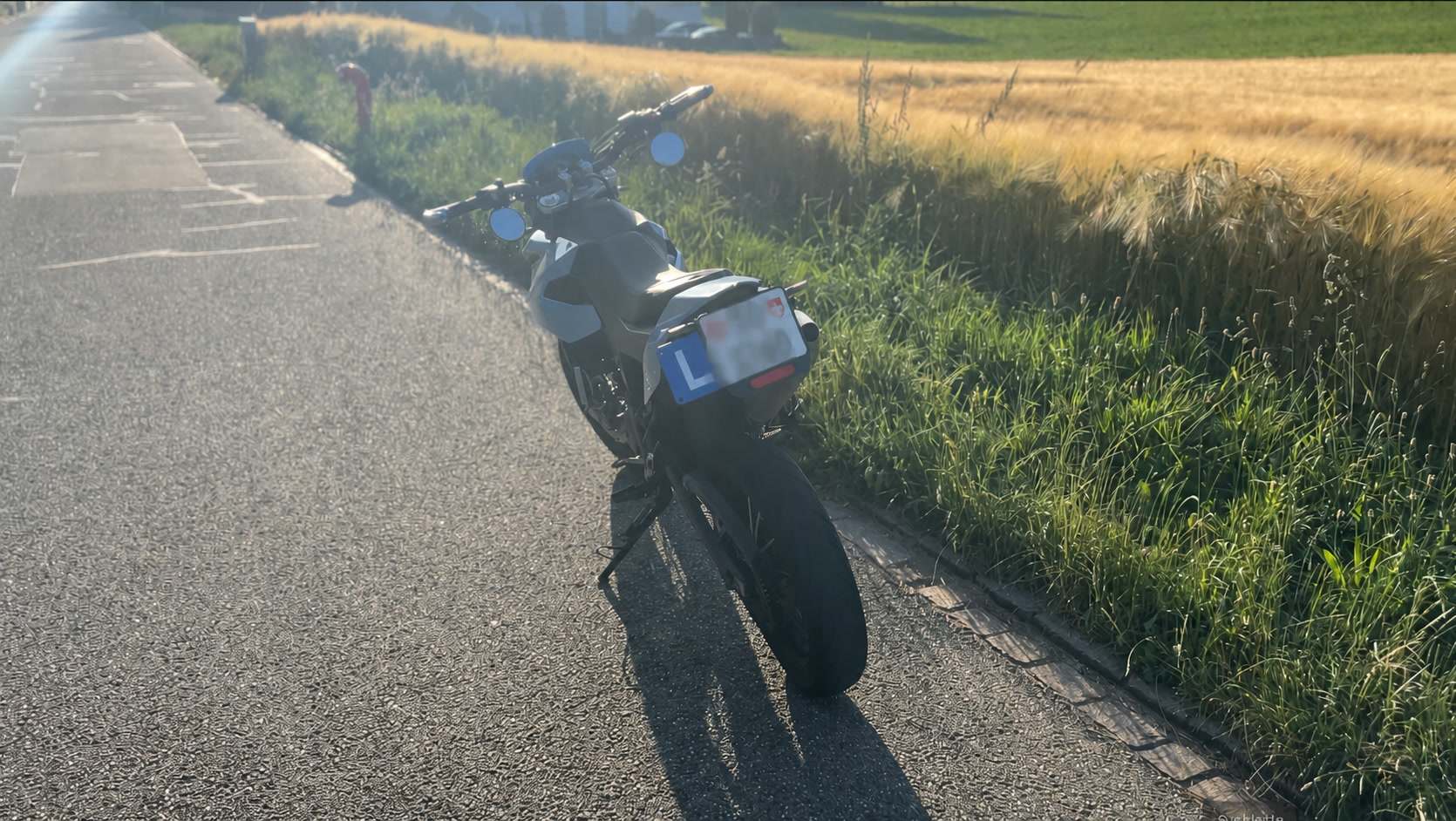 Blaues Aprilia-Motorrad von hinten auf einer Landstrasse neben einem Getreidefeld